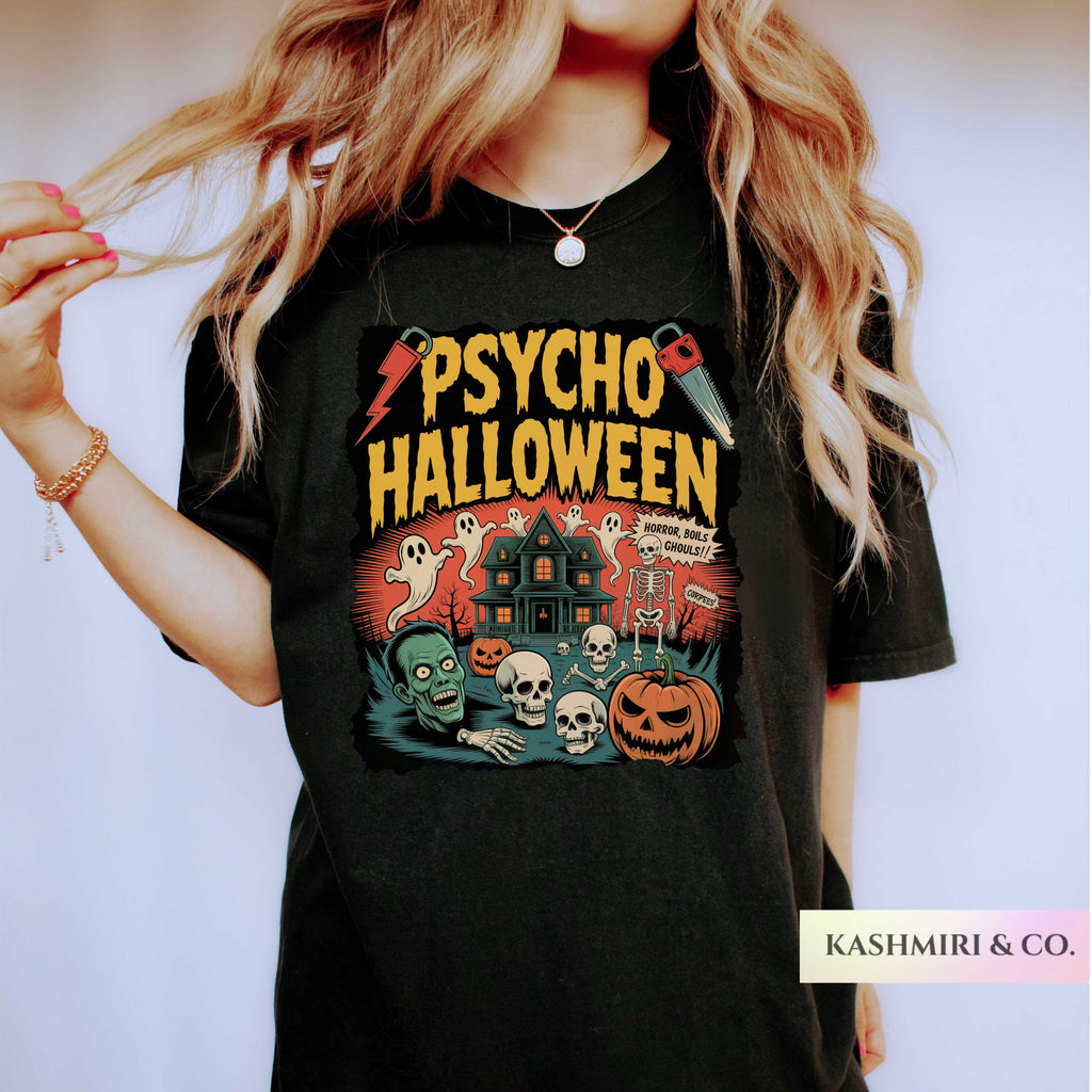 A woman wearing a black graphic t-shirt with a 'Psycho Halloween' print featuring a haunted house, skulls, pumpkins, and ghosts. The brand name 'KASHMIRI & CO.