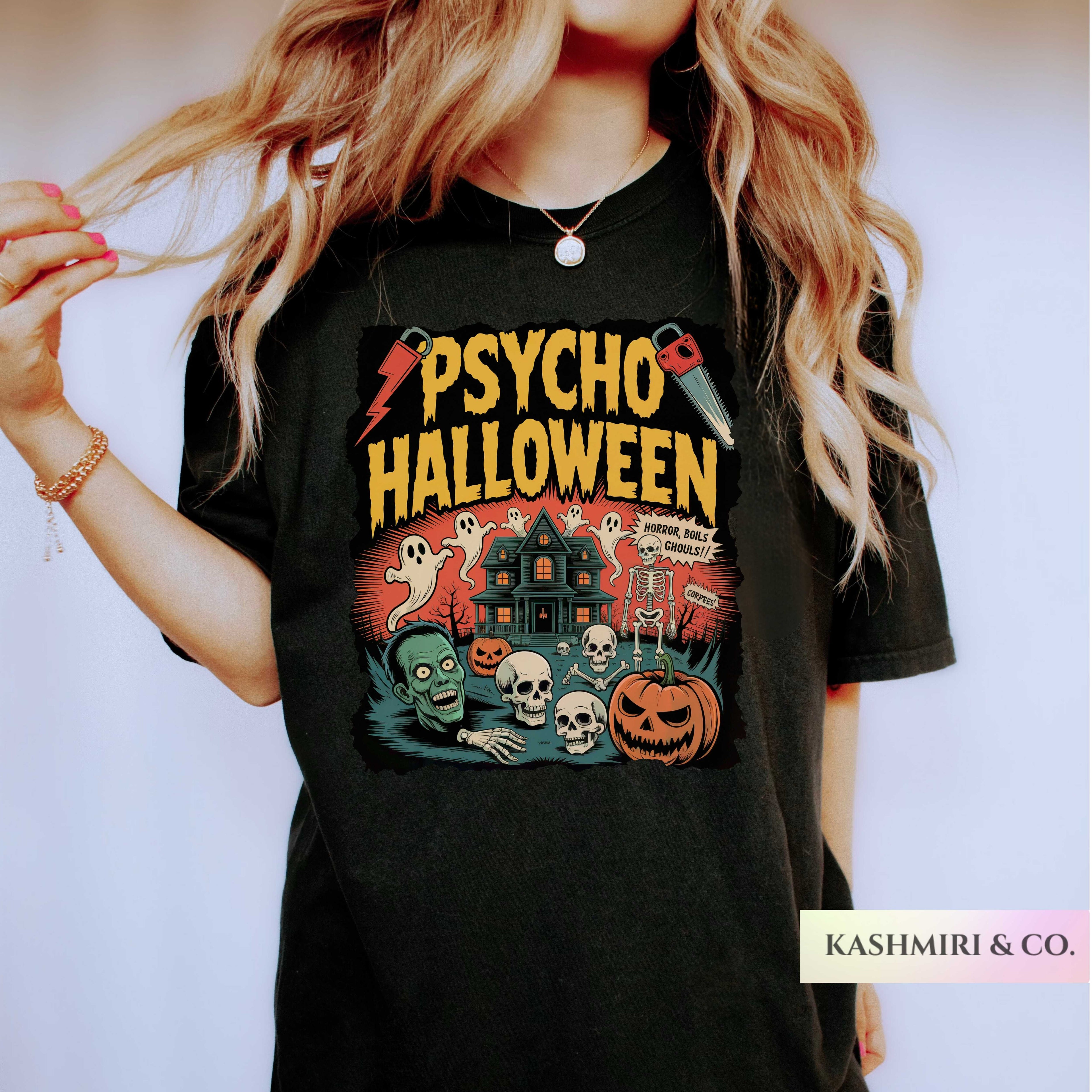 A woman wearing a black graphic t-shirt with a 'Psycho Halloween' print featuring a haunted house, skulls, pumpkins, and ghosts. The brand name 'KASHMIRI & CO.