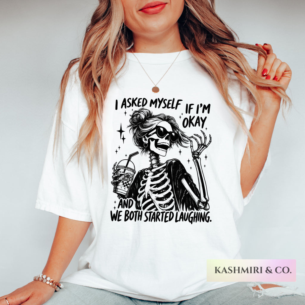A woman wearing a white graphic t-shirt with a black skeleton illustration and the text 'I ASKED MYSELF, IF I'M OKAY. AND WE BOTH STARTED LAUGHING.