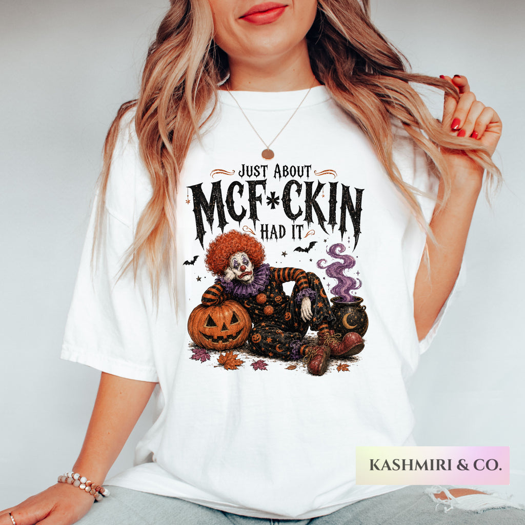 A woman wearing a white graphic t-shirt with a spooky clown and jack-o'-lantern design and the text 'JUST ABOUT MCF*CKINHAD IT'.