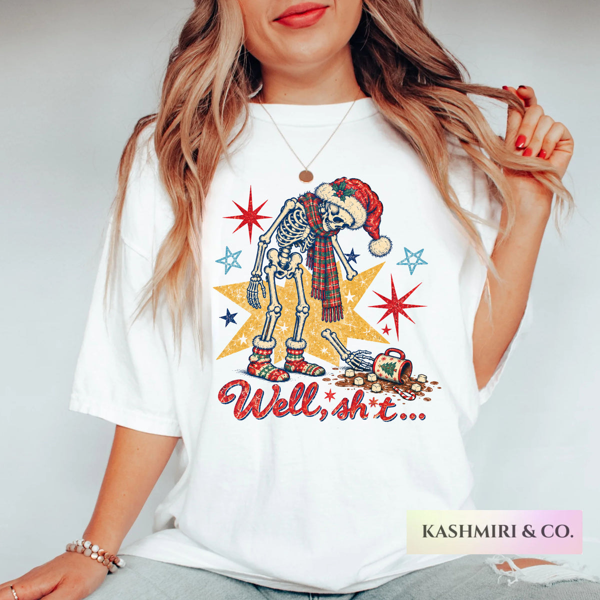 A woman wearing a white graphic t-shirt featuring a skeleton dressed in a Santa hat and scarf next to a gold star with the text 'Well, shit.