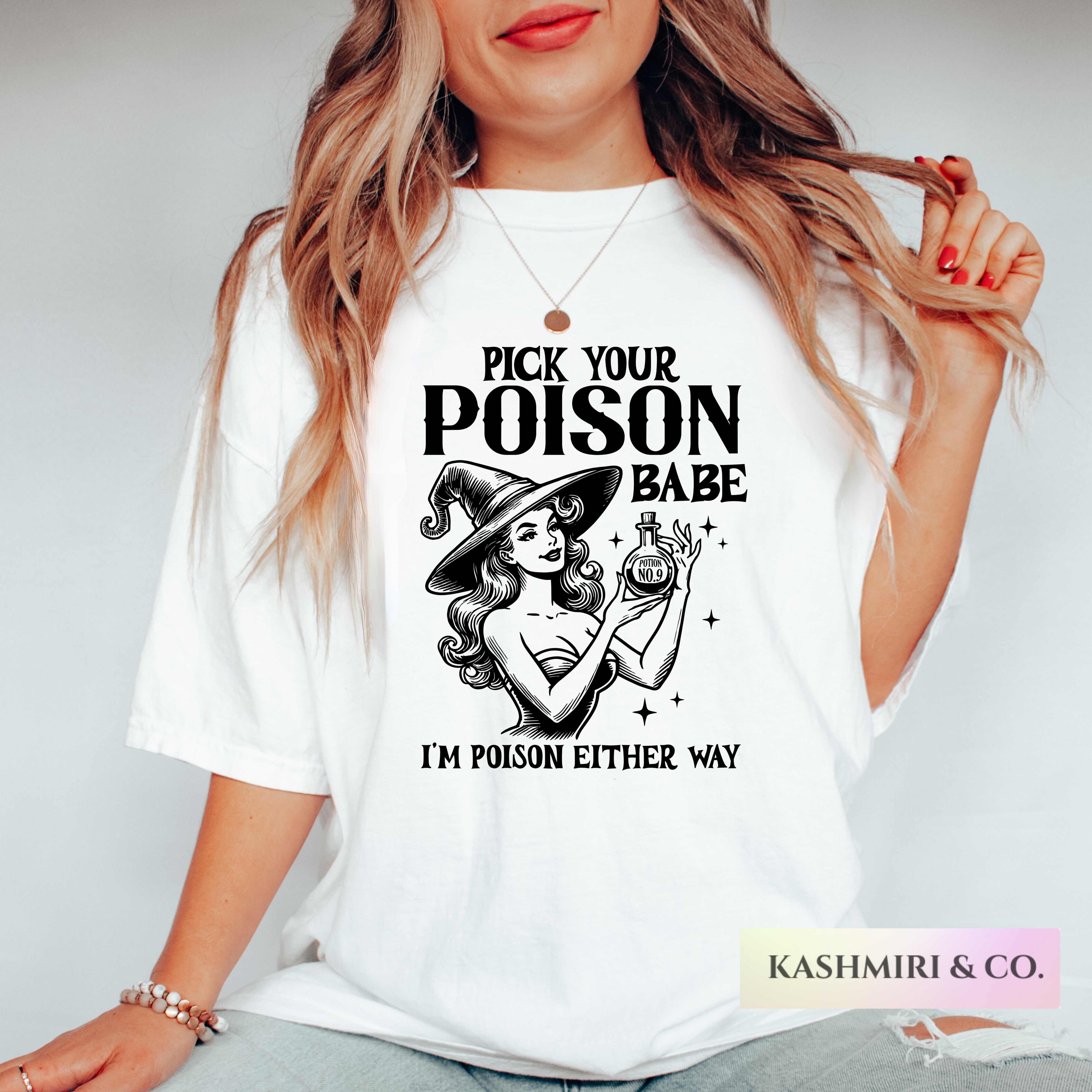 A woman wearing a white graphic t-shirt with a black print of a witch and the text 'PICK YOUR POISON BABE I'M POISON EITHER WAY'.