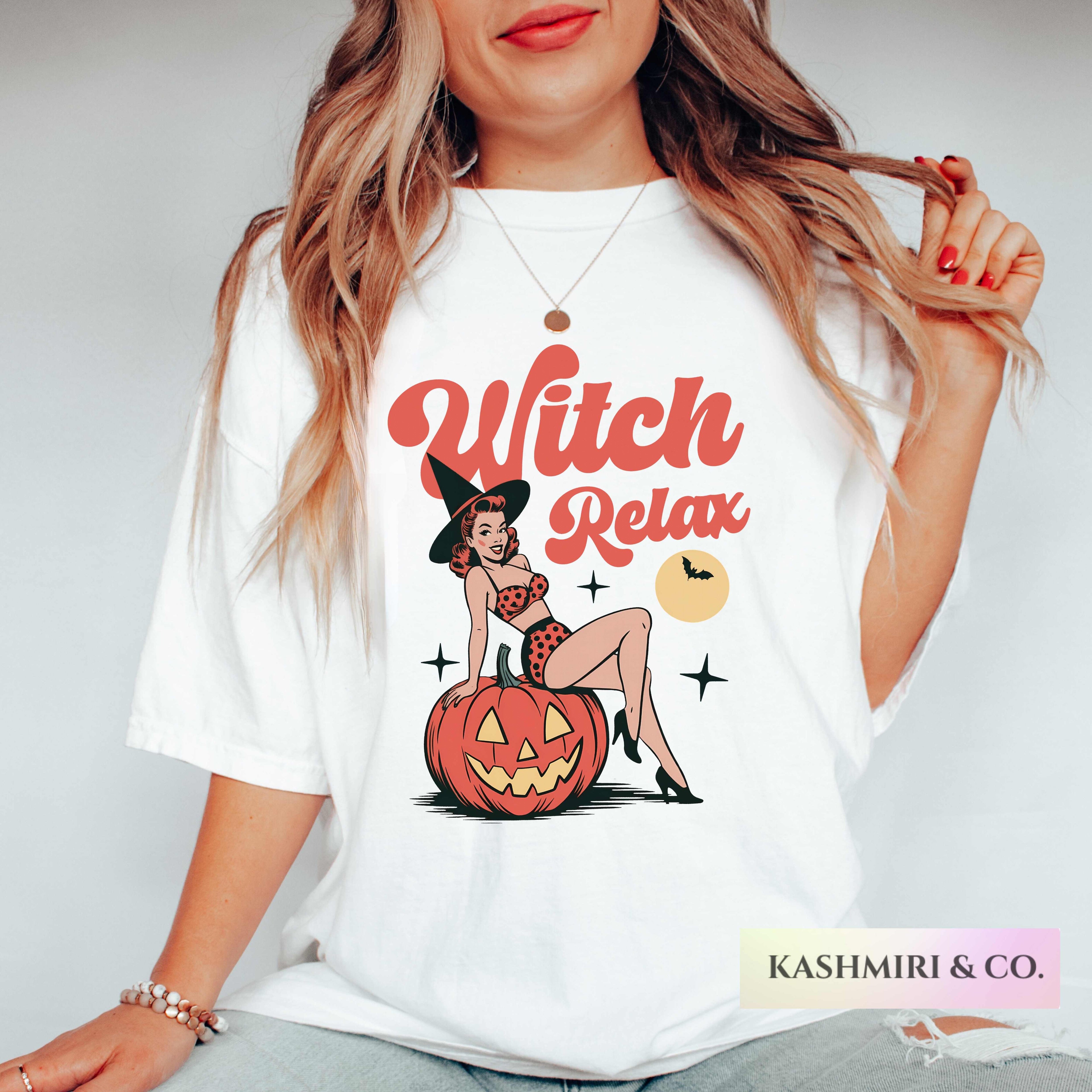 A woman wearing a white graphic t-shirt with a retro pin-up illustration of a witch sitting on a jack-o'-lantern and the words 'Witch Relax' in red script. The photo is cropped from the lips down, set against a plain light gray background.