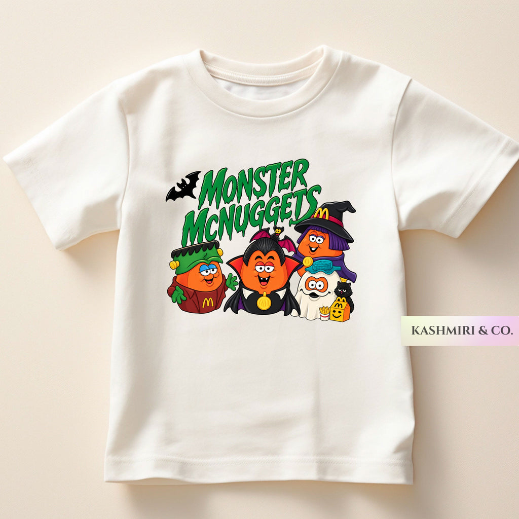 A white short-sleeve t-shirt with a colorful graphic print of cartoon McDonald's characters dressed as Halloween monsters under the text 'MONSTER McNUGGETS'. The characters include a green monster, a vampire, a witch, and a ghost.