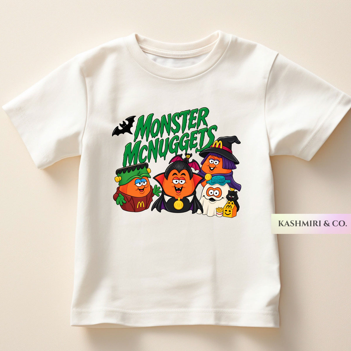 A white short-sleeve t-shirt with a colorful graphic print of cartoon McDonald's characters dressed as Halloween monsters under the text 'MONSTER McNUGGETS'. The characters include a green monster, a vampire, a witch, and a ghost.