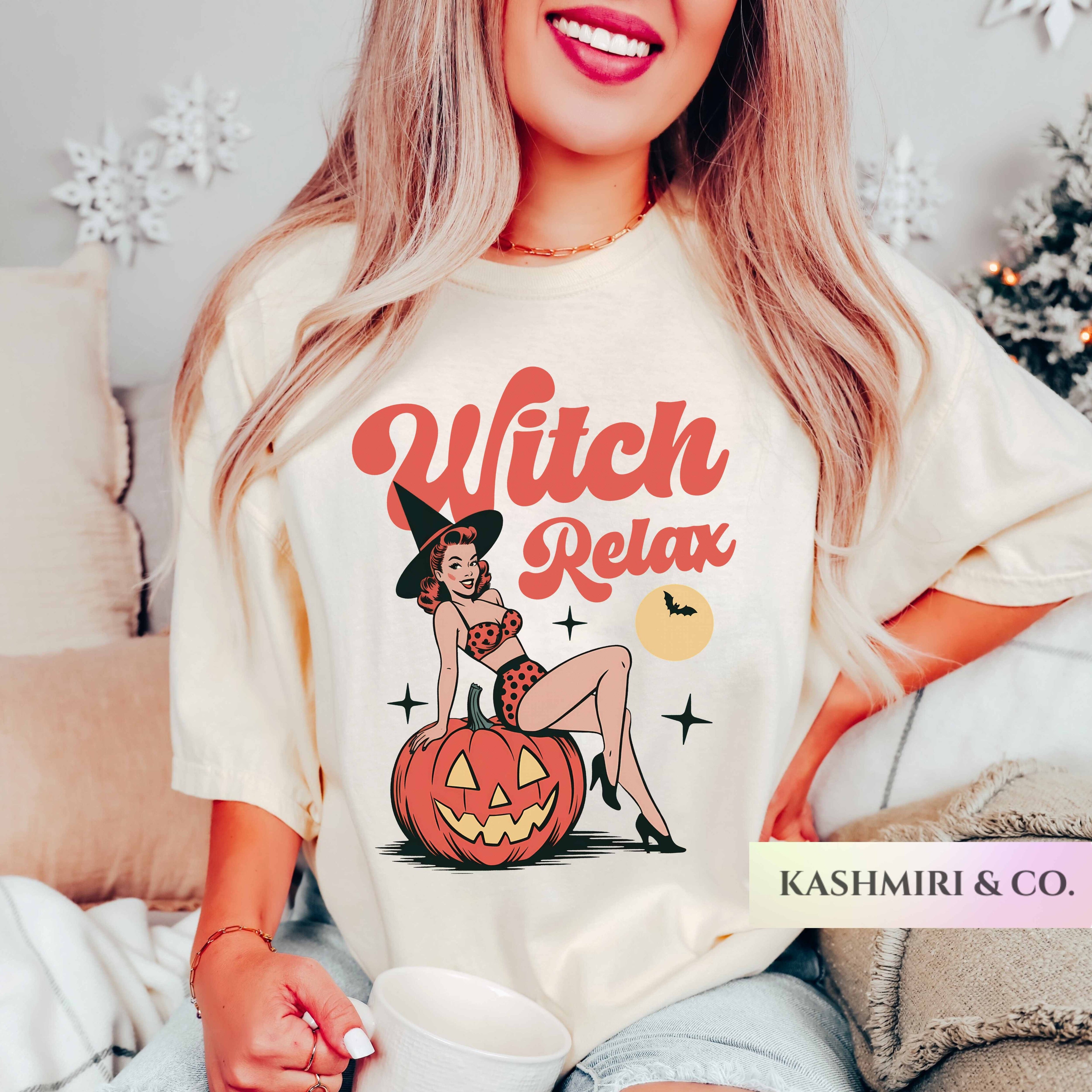 A woman wearing a cream-colored graphic t-shirt with a 'Witch Relax' Halloween design, sitting in a cozy indoor setting with a mug.