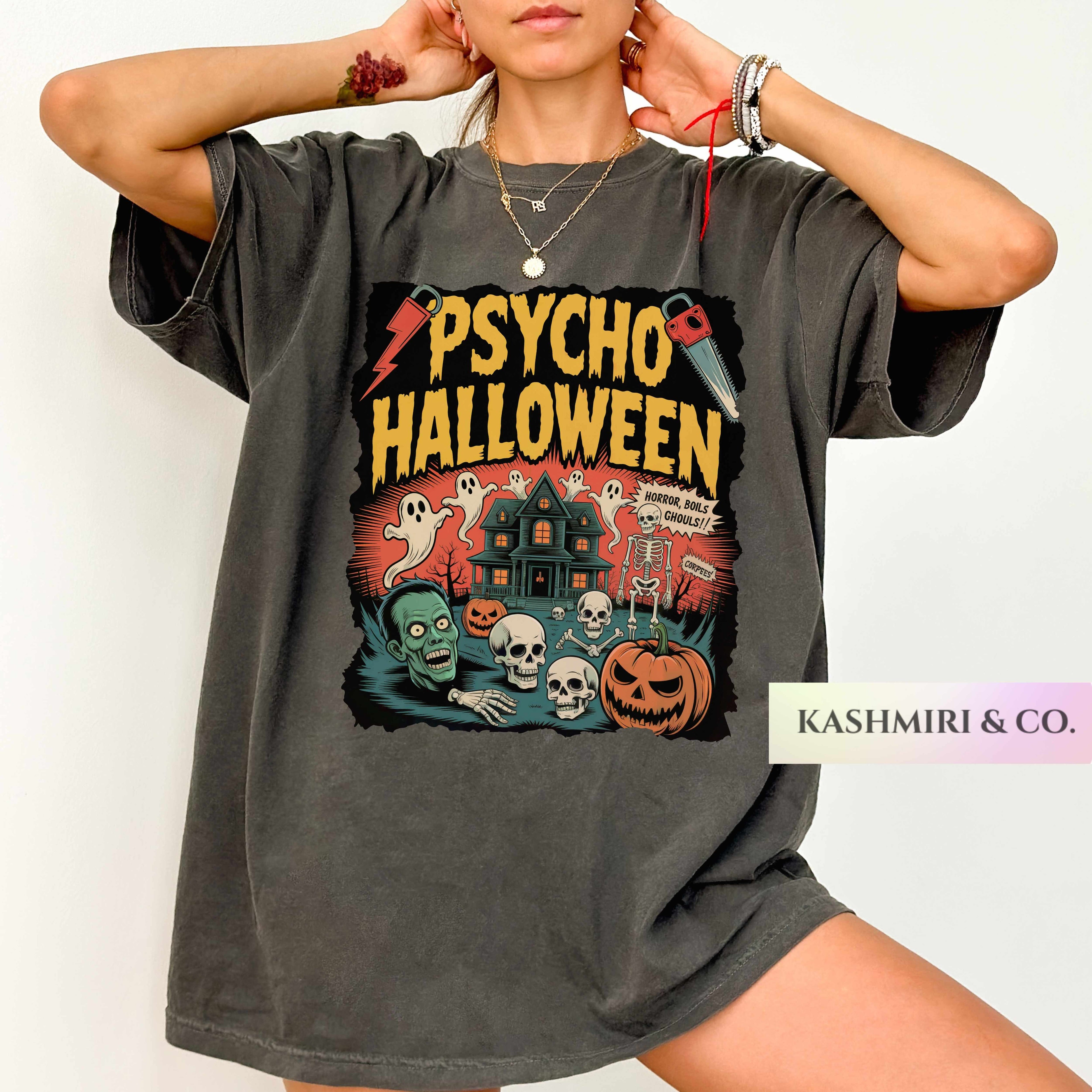 A woman wearing an oversized dark gray t-shirt with a colorful 'Psycho Halloween' graphic print, posed against a plain white background. A brand label 'KASHMIRI & CO.