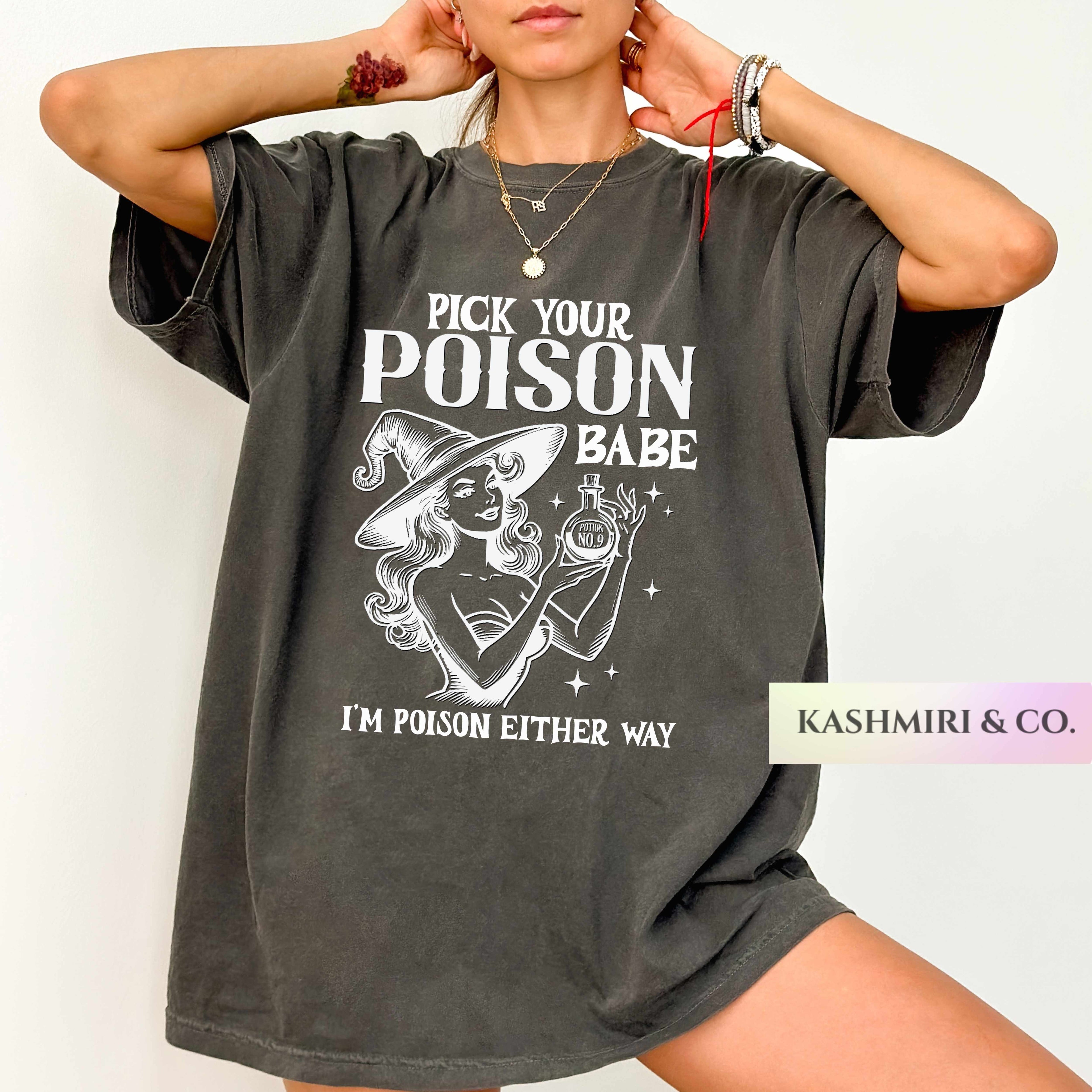 A woman wearing an oversized dark gray graphic t-shirt with a white print that reads 'PICK YOUR POISON BABE I'M POISON EITHER WAY' and features an illustration of a witch holding a poison vial. A brand label 'KASHMIRI & CO.