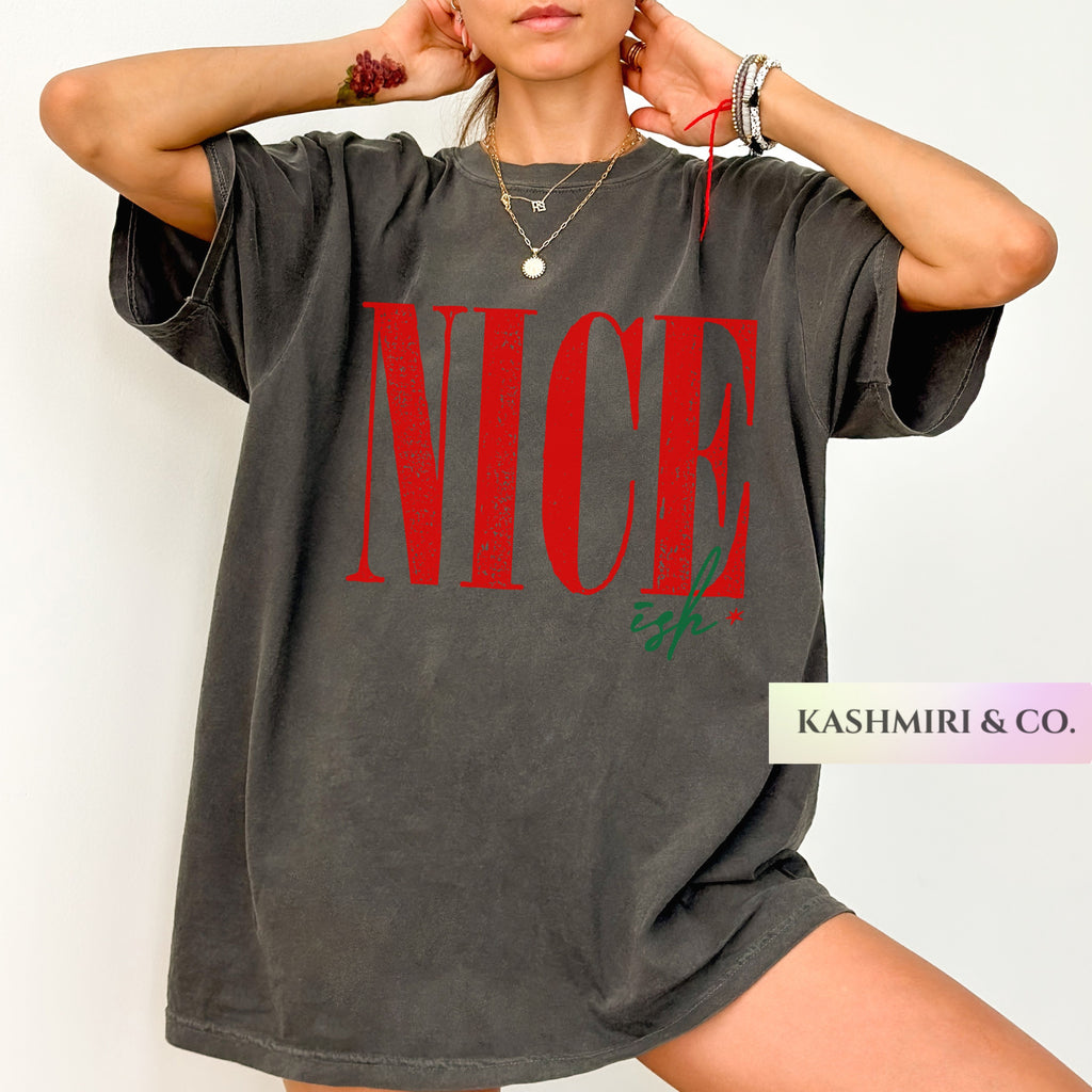 A woman wearing an oversized faded charcoal gray t-shirt with 'NICE' printed in red and 'ish.' in green script across the front.