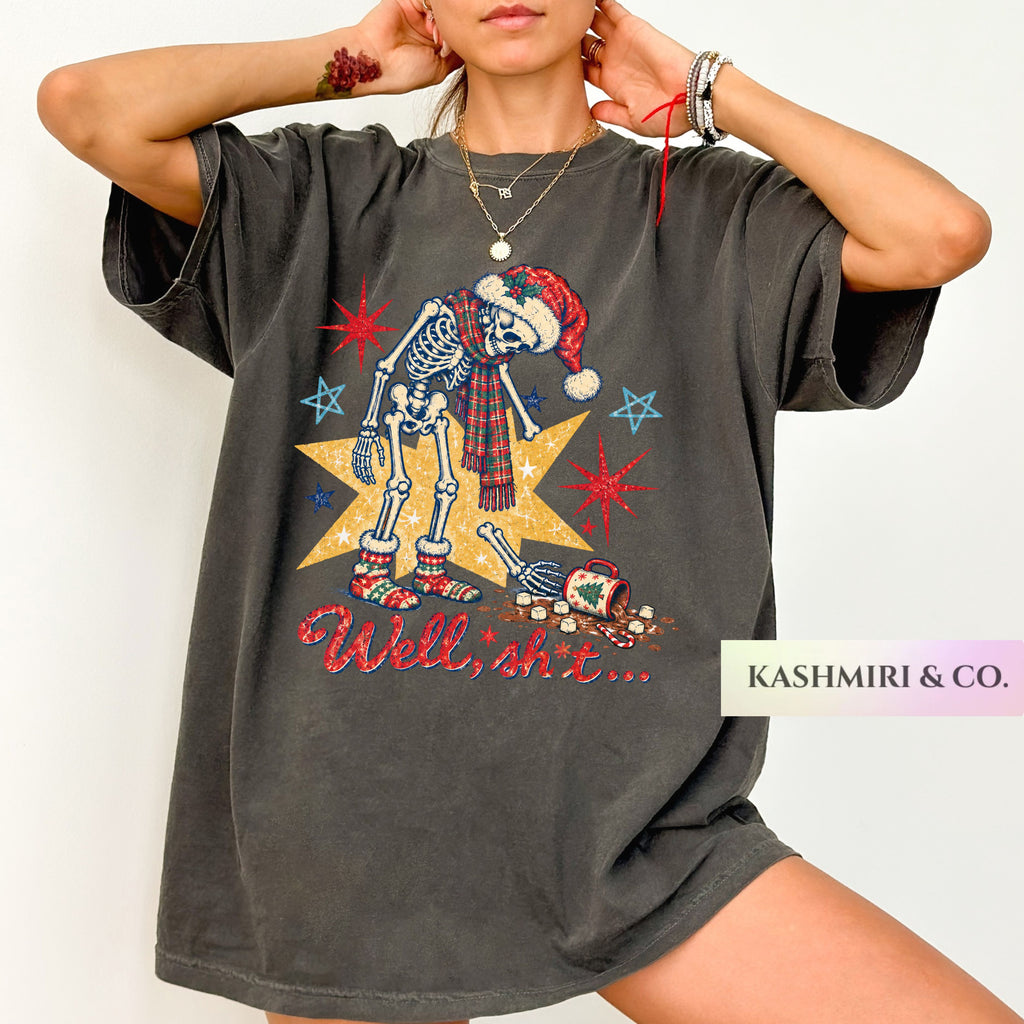 A woman wearing an oversized dark gray graphic T-shirt with a festive skeleton wearing a Santa hat and plaid scarf, standing on a yellow star with the text 'Well, shit.