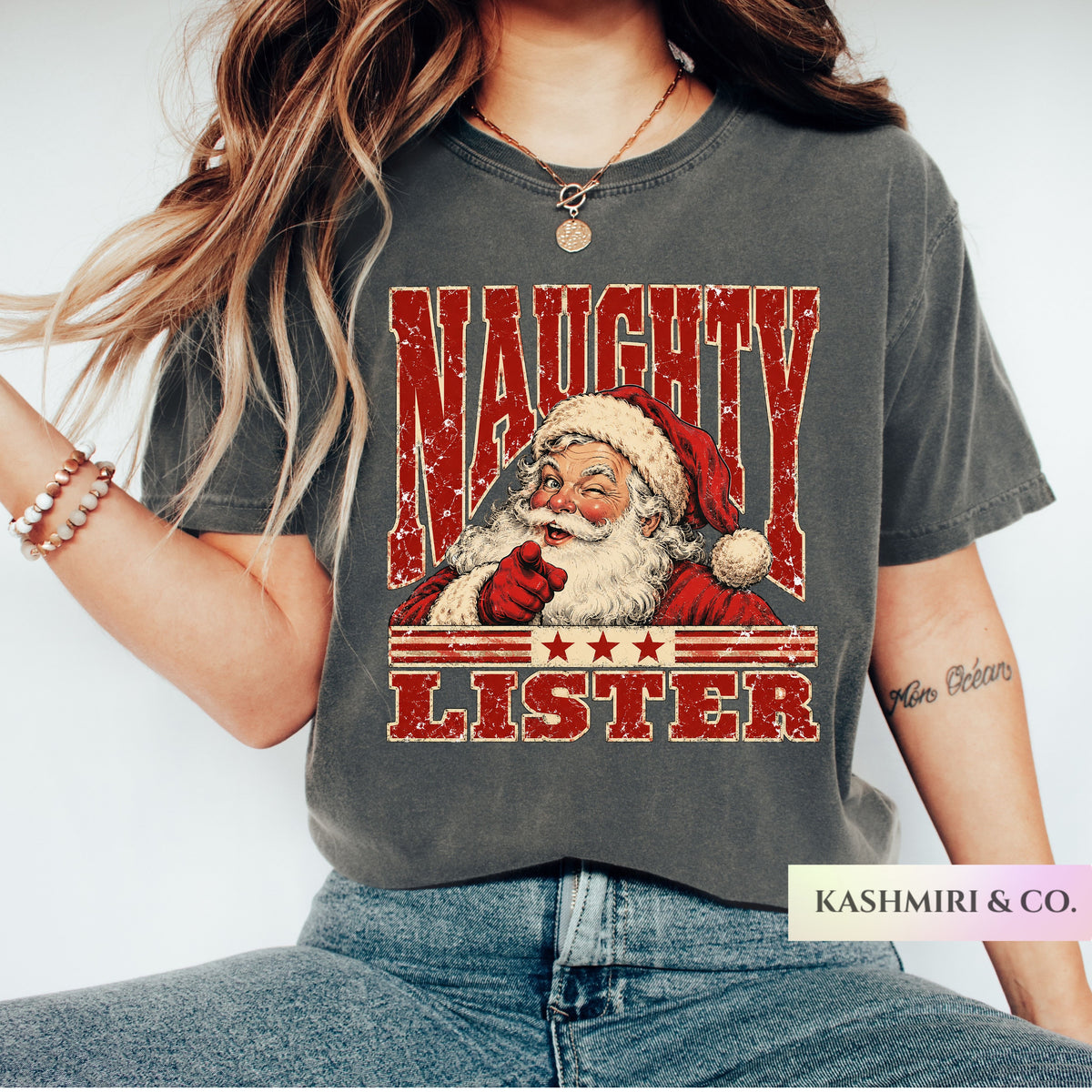A woman wearing a dark gray graphic t-shirt with a distressed red and white print of Santa Claus and the text 'NAUGHTY LISTER'.