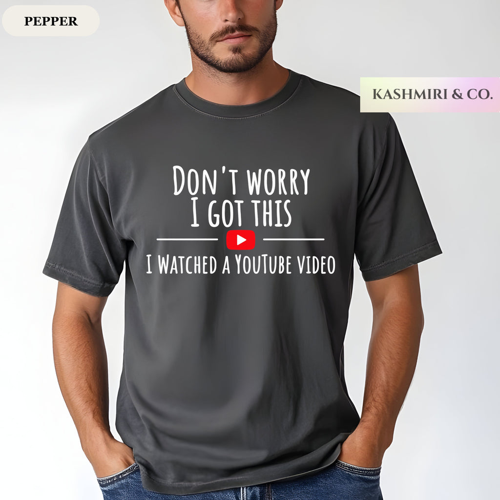 A man wearing a dark gray 'pepper' t-shirt with a white graphic text print that reads 'DON'T WORRY I GOT THIS I WATCHED A YOUTUBE VIDEO' with a red play button icon. The brand 'KASHMIRI & CO.